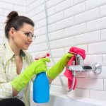 Woman in gloves with detergent and rag doing bathroom cleaning
