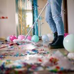 Woman with pushbroom cleaning mess of floor in room after party confetti